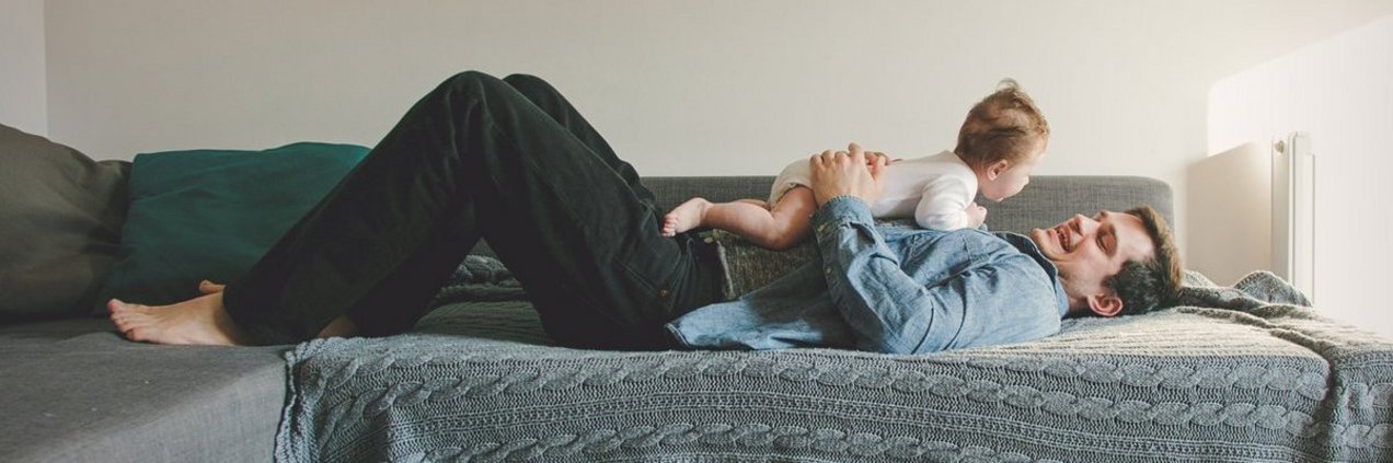 Vater mit Baby im Arm auf dem Sofa